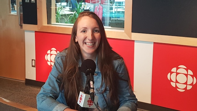 Une jeune femme au cheveux bruns et longs, très souriante qui se trouve dans un studio.