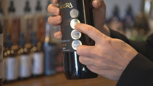 Une main tient une bouteille de vin sur laquelle un sceau signale l'obtention d'un prix à un concours.