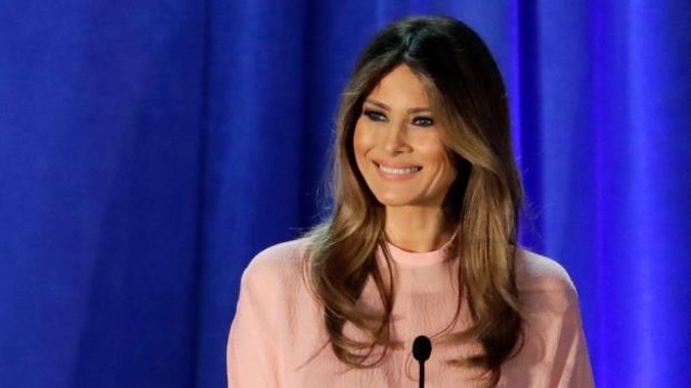 Melania Trump souriant devant un micro avec une chemise rose pâle