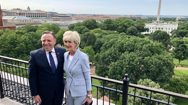 François Legault et Isabelle Brais posent sur un balcon, la Maison-Blanche apparaît en arrière-plan.