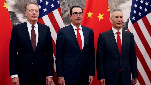 Trois hommes portant des vestons de couleur bleu marin et des cravates rouges posant devant les drapeaux américain et chinois.