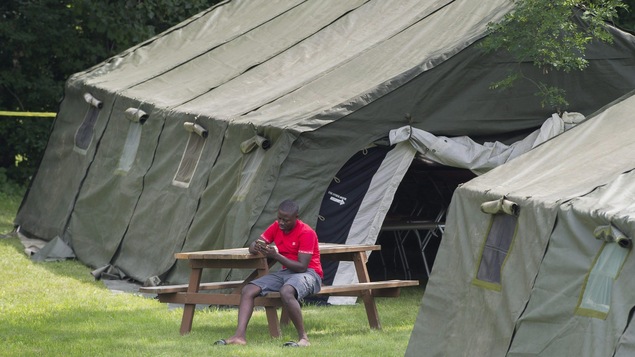 Un homme assis à une table consulte son téléphone, dans un campement. Un homme assis à une table consulte son téléphone, dans un campement.