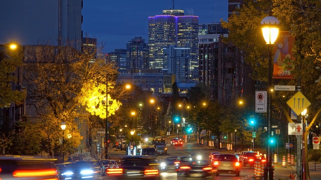 Des voitures circulent sur la route, alors que le jour se lève sur le centre-ville de Montréal.