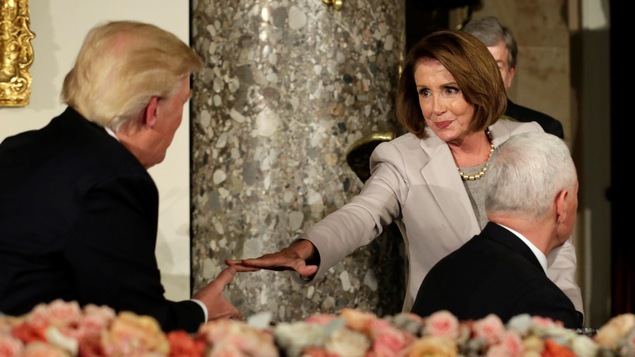 Nancy Pelosi tend la main en direction de Donald Trump, qui s'apprête à la serrer.