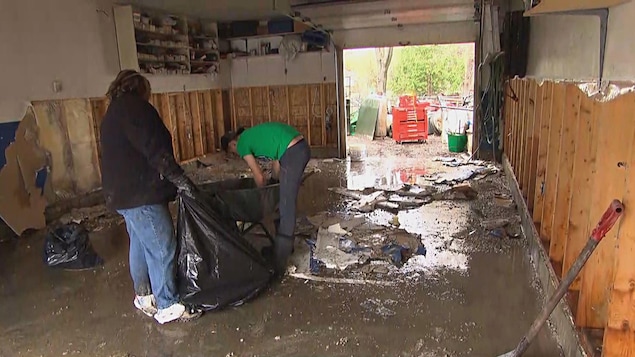 Deux personnes ramassent des débris de démolition dans un garage qui a été inondé. Deux personnes ramassent des débris de démolition dans un garage qui a été inondé.