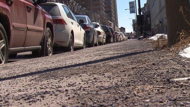 Un trottoir plein de roches côtoie une file de voitures stationnées.