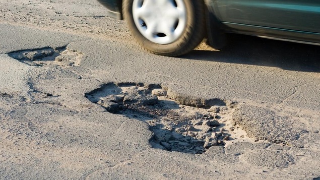 Une voiture évite un nid de poule.