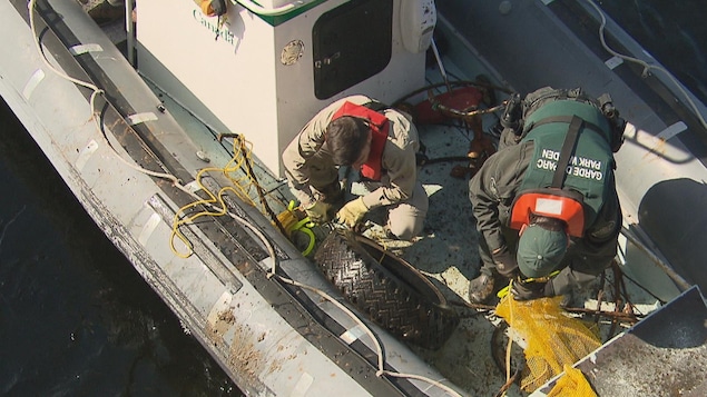 Deux hommes sur une embarcation sortent des objets du fjord