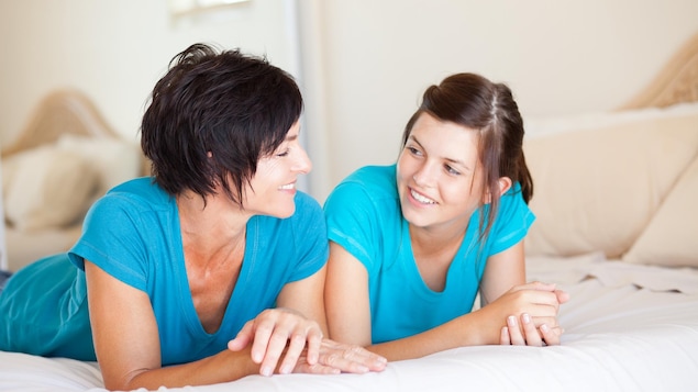 Une mère et son adolescente sont étendues sur un lit et se regardent en souriant.