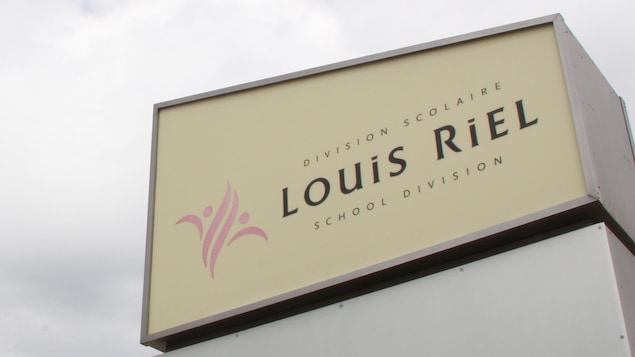 L'insigne de la Division scolaire Louis-Riel contre un ciel nuageux. 