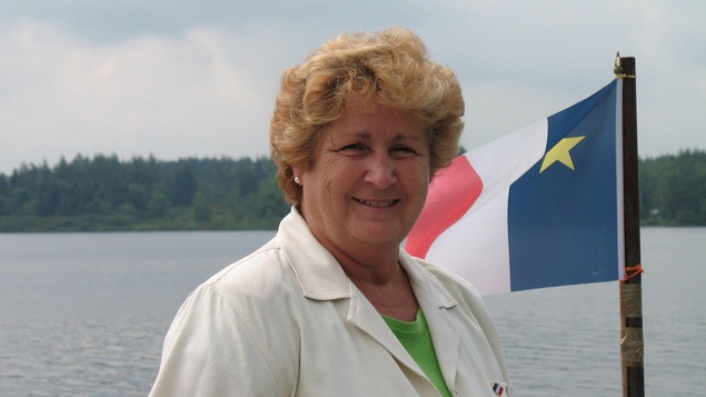 Paulette Sonier Rioux pose devant un plan d'eau et le drapeau acadien.