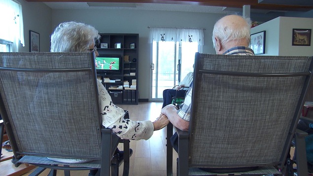Un couple âgé se tenant par la main en regardant le soccer à la télévision.