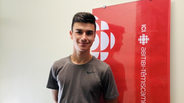 Un jeune homme devant une affiche de Radio-Canada.
