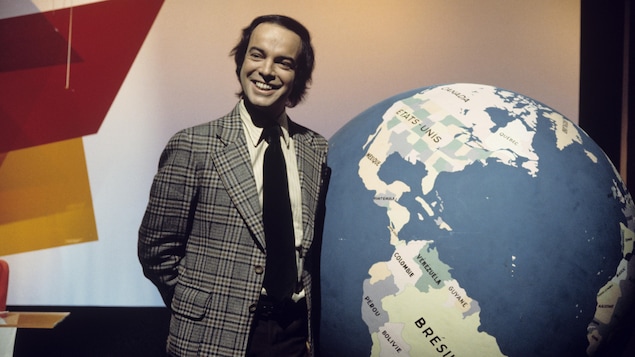 Dans un studio de télévision, Pierre Nadeau est debout, souriant, devant
un gros globe terrestre.