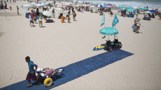 Un tapis posé sur une plage de Rio de Janeiro, où un jeune homme tire une personne en fauteuil roulant.