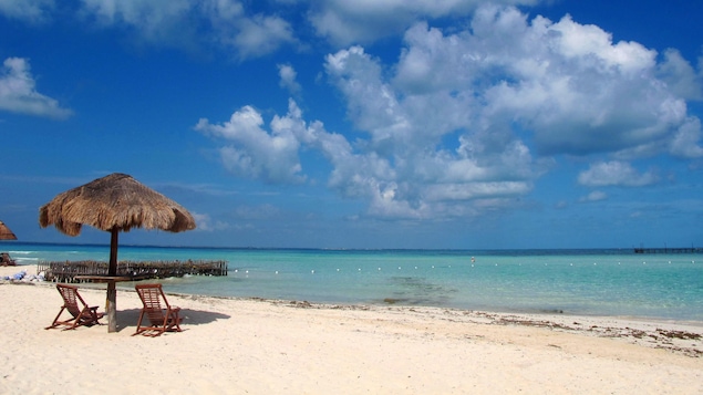 Photo de deux chaises et d'un parasol sur une plage du Mexique sous le ciel bleu