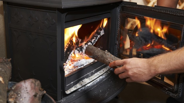 Une personne met une bûche dans un poêle à bois. Une personne met une bûche dans un poêle à bois.
