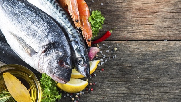 Des poissons et des crevettes crus reposent sur un plan de travail en bois.