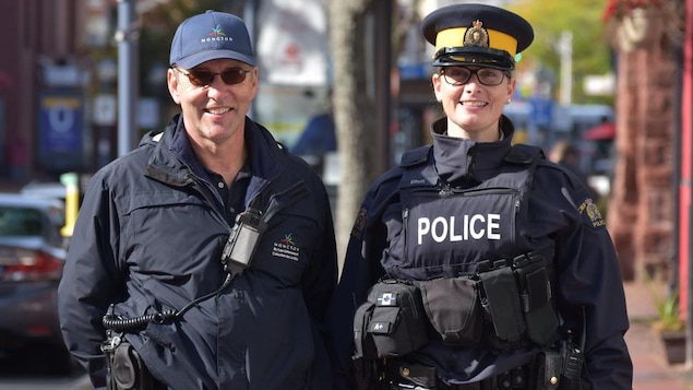Un homme et une femme en uniforme côte à côte sur un trottoir.