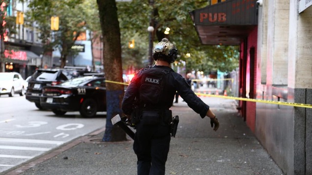 Un policier marche dans le quartier Downtown Eastside à Vancouver. Un ruban jaune encercle un parti du trottoir. 