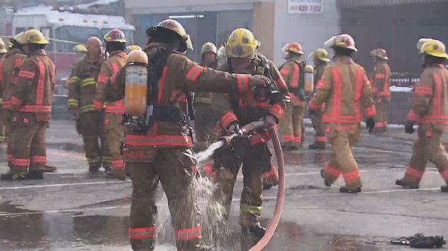 Un pompier qui arrose un autre pompier pour décontaminer sa combinaison sur le site d'un incendie à Montréal