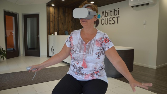 Une femme porte un casque de réalité virtuelle et tient ses mains levées, comme si elle touchait quelque chose.