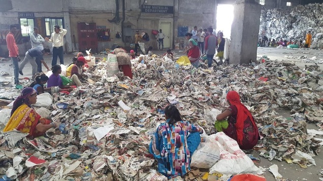 Des travailleuses indiennes assises par terre sur des amoncellements de papier.
