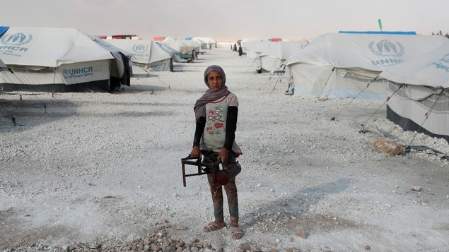 Une adolescente tient un brûleur pour faire la cuisine en plein milieu d'un camp de déplacés à Raqqa, en Syrie. Des tentes l'entourent. Une adolescente tient un brûleur pour faire la cuisine en plein milieu d'un camp de déplacés à Raqqa, en Syrie. Des tentes l'entourent.
