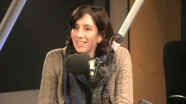 Une jeune dame assise derrière un micro dans un studio radio