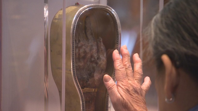Une femme touche une vitrine contenant une main et avant-bras momifiés