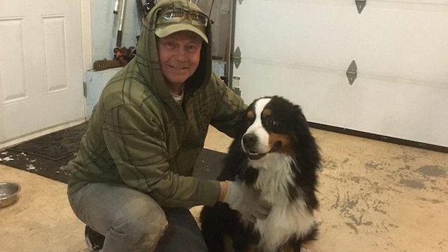 Un homme est agenouillé et tient un chien de race bouvier bernois.