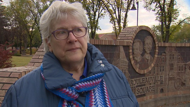 Suzanne de Courville Nicole est devant le parc de Rouleauville. Elle a des cheveux blancs et des lunettes.