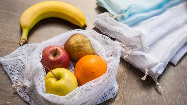 Un petit sac en tissu contient plusieurs fruits (pommes, orange, poire, banane).