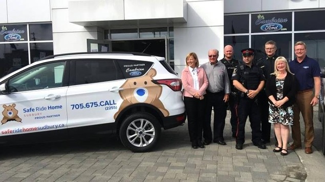 Un groupe de personnes à côté d'une voiture portant le logo de Safe Ride Home Un groupe de personnes à côté d'une voiture portant le logo de Safe Ride Home