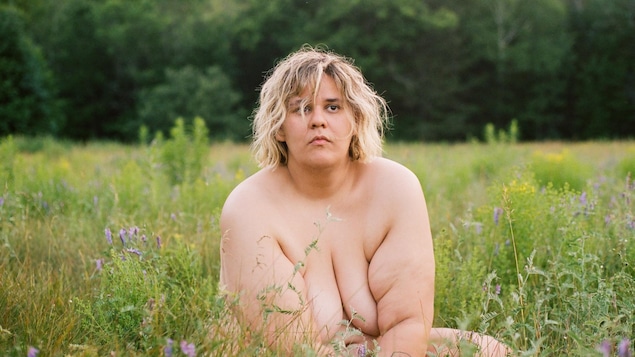 L'artiste est assise nue dans l'herbe.