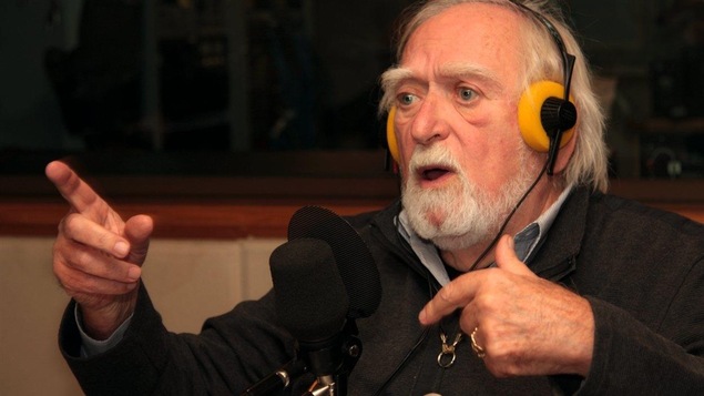 Jacques Languirand avec des écouteurs sur la tête pointe du doigt, dans un studio de radio de Radio-Canada.