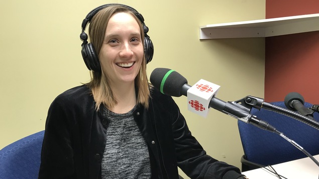 Une femme sourit à la caméra derrière un micro de Radio-Canada.