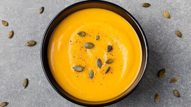 Un bol de soupe de courge parsemé de sel, de poivre et de graines de courge