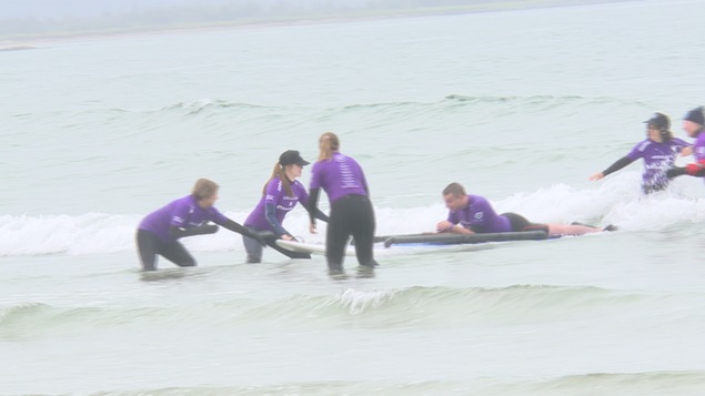 Des bénévoles aident un homme faisant du surf couché sur sa planche