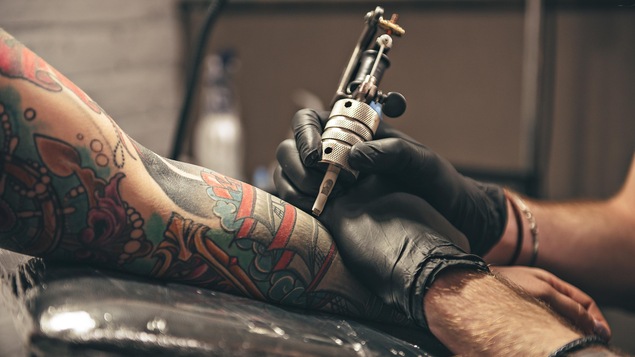 Une personne qui tient un outil permettant de faire des tatouages fait un dessin sur le bras d'une autre personne.