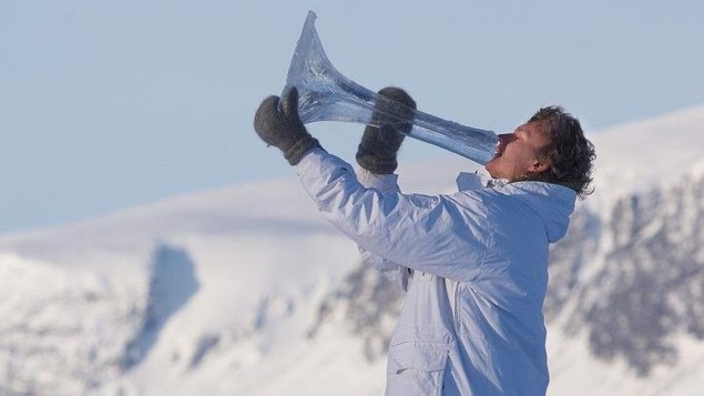 Un homme chaudement habillé souffle dans une énorme trompette transparente. L'angelot des neiges se trouve dans quelque paysage montagneux.