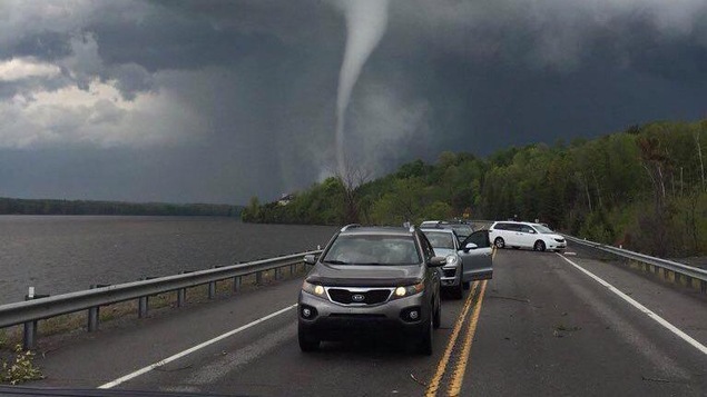Une file de voitures et derrière une tornade.