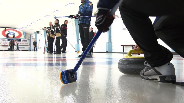 Lancement d'une pierre de curling alors que d'autres joueurs observent.