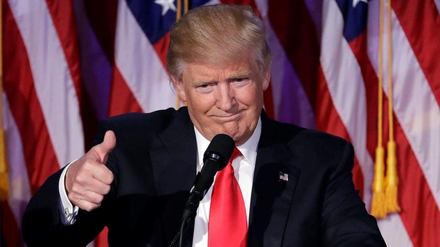 Donald Trump avec le pouce en l'air devant des drapeaux.