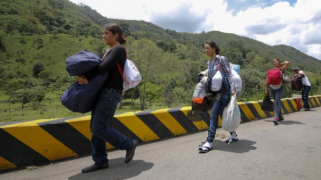 Trois femmes et un homme chargés de sacs marchent sur la route.