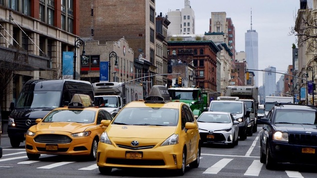 Rue bondée de Manhattan, taxis en avant-plan vus de face et voitures, édifices en arrière-plan.