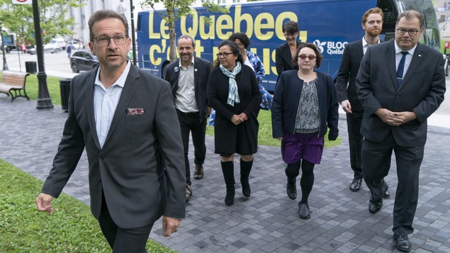 Yves-François Blanchet marche tout près de son autobus de campagne. Il est suivi par plusieurs personnes.