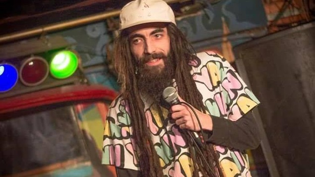 L'homme barbu porte une casquette et tient un micro.