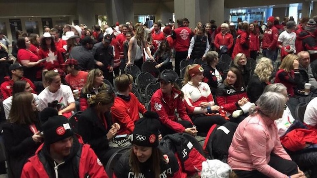 Des athlètes canadiens vêtus de vêtements aux couleurs du Canada sont réunis devant le salle du conseil municipal de la ville de Calgary.