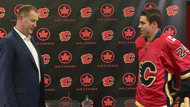 Travis Hamonic enfile son nouveau chandail sous l’œil attentif du directeur général des Flames, Brad Treliving